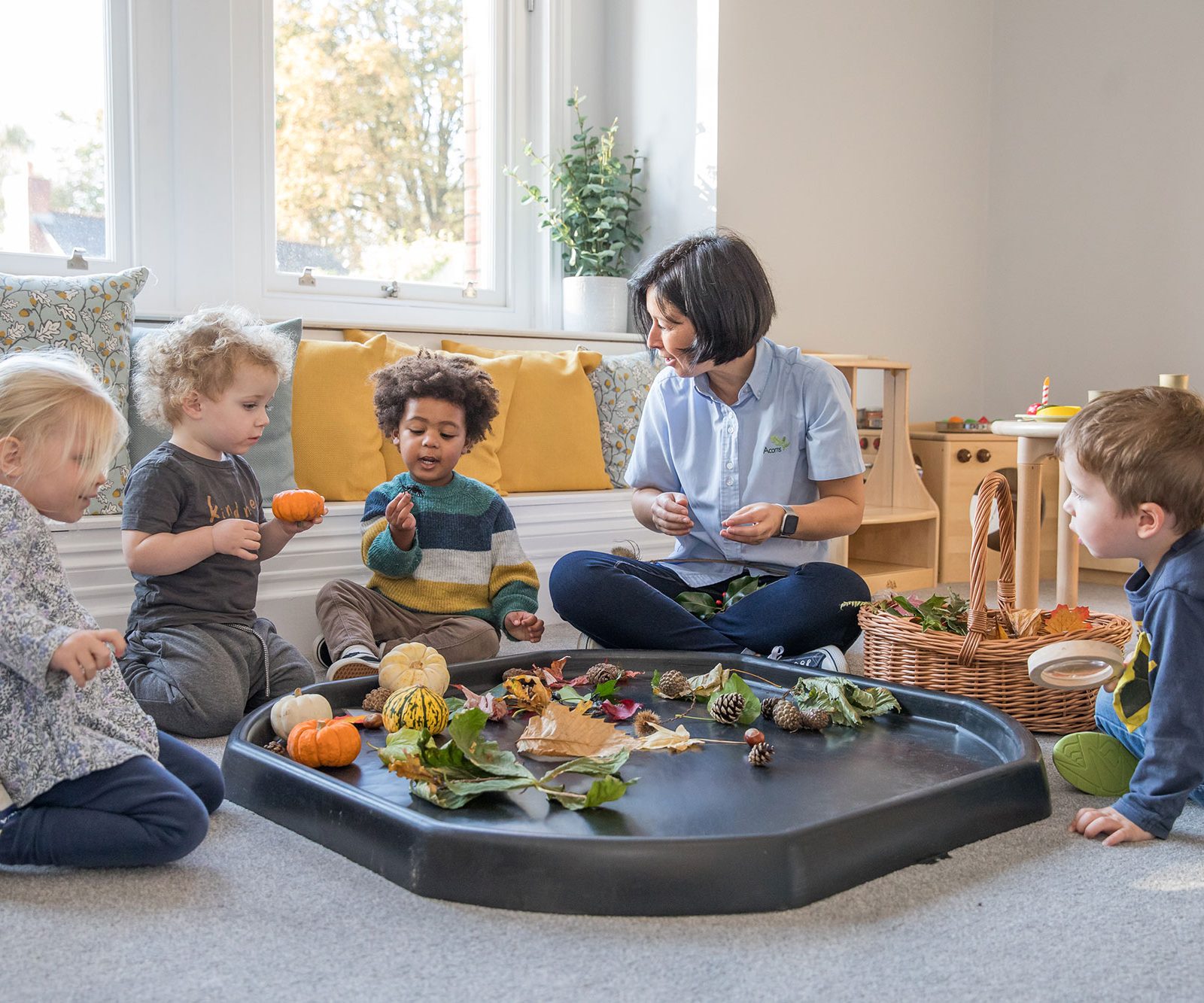 Acorns Nurseries Children sitting with an adult in a bright room in Llandaff, engaged in an autumn-themed activity with leaves, acorns, and small pumpkins.