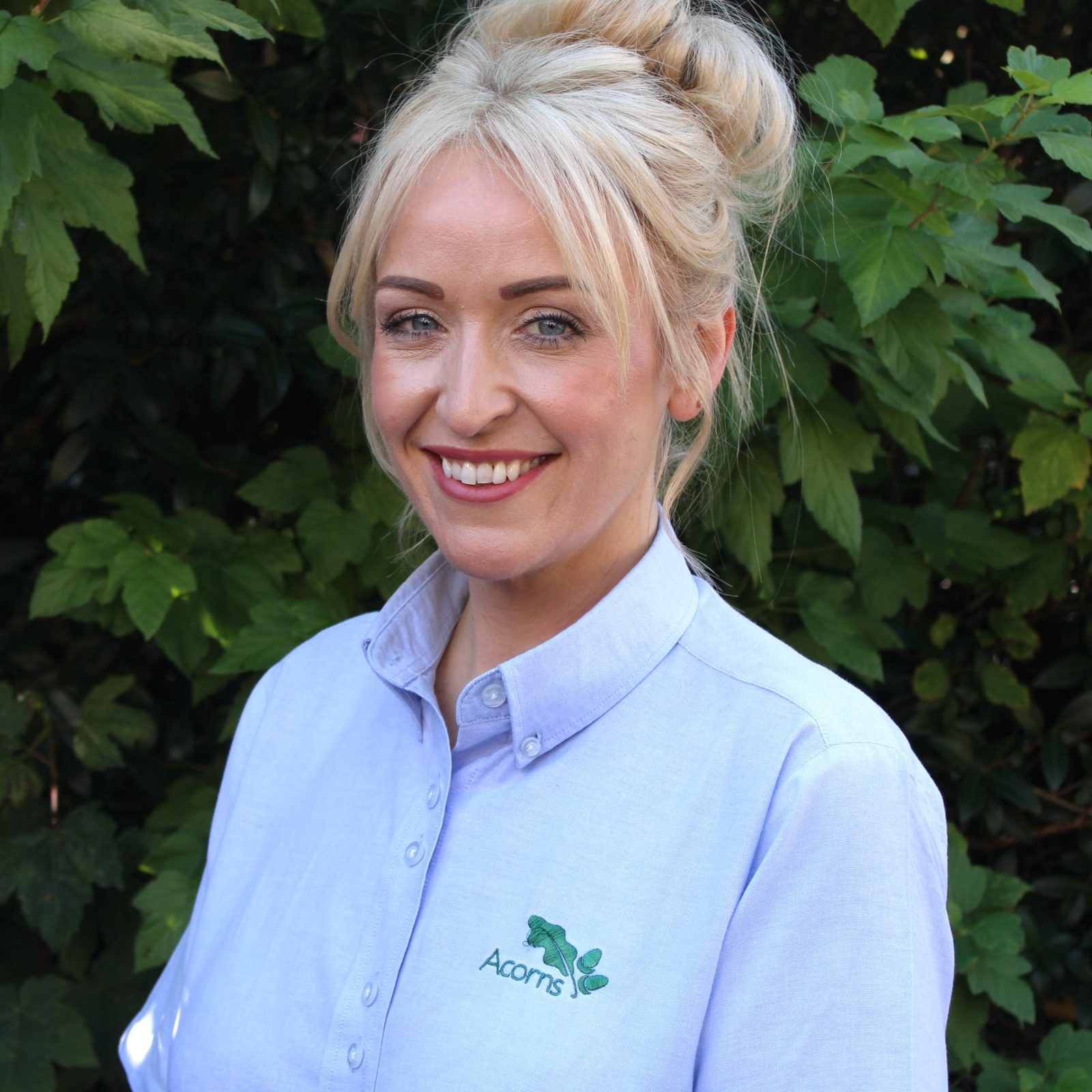 Acorns Nurseries Woman with blonde hair in a bun, wearing a light blue 